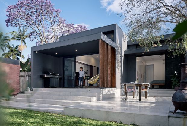Contemporary single-storey residence viewed from the landscaped rear garden, with a broad stepped concrete terrace and outdoor entertaining area. The dark charcoal facade includes flat roof forms, large glazed openings, and a prominent vertical timber screen dividing the covered outdoor room from the adjacent living space. Tropical and flowering garden planting surrounds the house, while outdoor dining furniture and a freestanding fire vessel sit on the terrace.