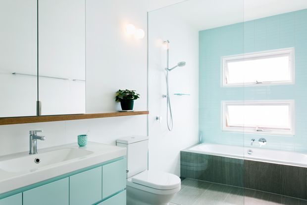 Bright contemporary bathroom with a wall-mounted vanity, integrated basin, mirrored cabinetry, walk-in shower, toilet, and freestanding-style bathtub. The room features pale turquoise wall tiles, white fixtures, grey tiled flooring, and warm timber trim accents.