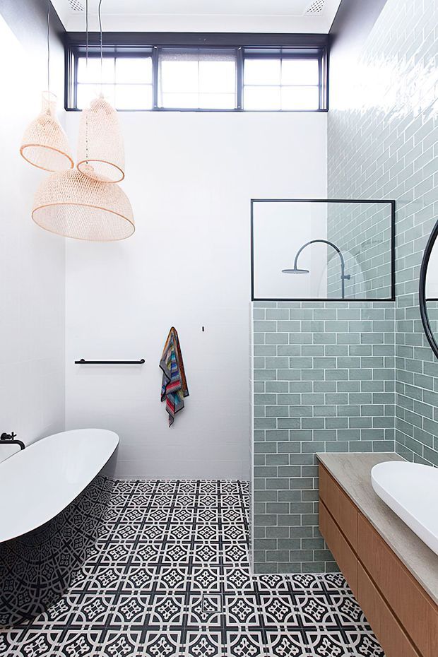 Bright contemporary bathroom with a freestanding white bathtub, patterned black-and-white floor tiles, pale green subway-tile shower wall, timber vanity with a light stone benchtop, black-framed windows and shower screen, and sculptural woven pendant lights.