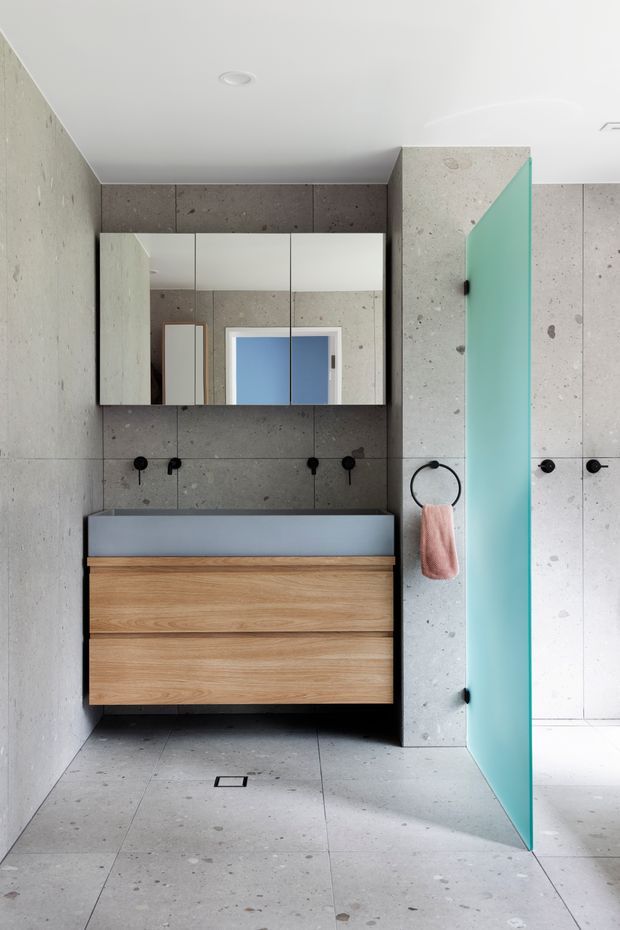 Contemporary bathroom with large grey concrete-look wall and floor tiles, a floating natural timber vanity with a grey basin, mirrored wall cabinets, matte black tapware and fixtures, and a distinctive translucent turquoise glass shower screen.