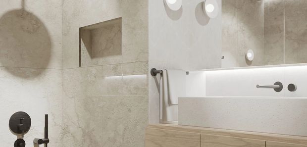Contemporary bathroom interior featuring large pale stone-look wall tiles, a recessed wall niche, brushed dark metal fixtures, a wall-mounted basin with integrated backsplash, and light timber vanity cabinetry. A large mirror with circular wall lights and concealed under-mirror illumination enhances the clean, refined design.