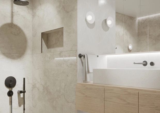 Contemporary bathroom with pale stone-look wall surfaces, a walk-in shower, recessed niche, wall-mounted controls, a large mirror, rounded wall lights, and light timber vanity cabinetry. The restrained palette and integrated lighting create a clean, refined atmosphere.