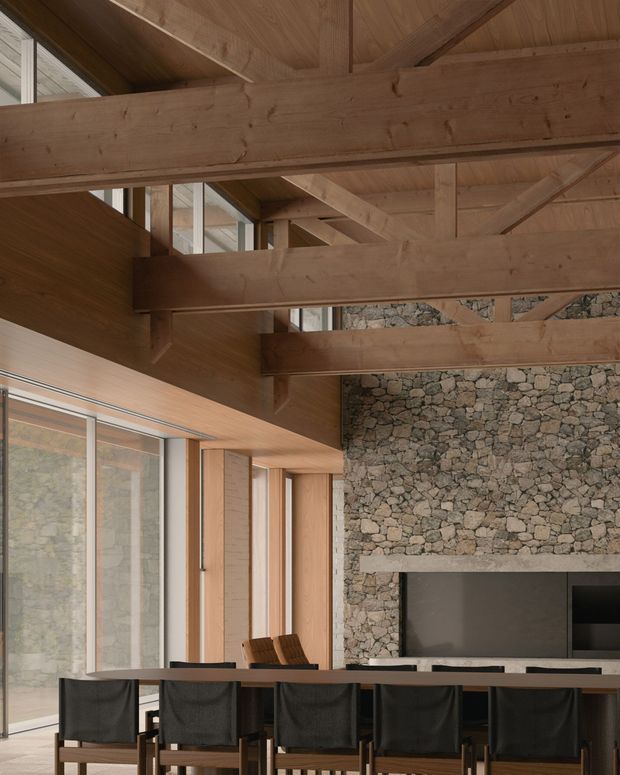 A warm, double-height dining and living space with a long dark dining table and upholstered dining chairs in the foreground. Exposed timber beams and timber-lined ceilings span the room, while a large rough-stone fireplace wall forms the focal point. Full-height glazing and timber-framed openings bring in natural light, with additional timber wall panelling and built-in joinery visible around the fireplace.