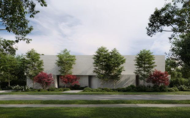 A low, wide modern building viewed from across a quiet street, partially screened by mature trees and landscaped garden beds. The facade is composed of pale horizontal cladding or masonry, with deep recessed openings and a simple flat roofline. Red-leaf ornamental trees provide accents against the restrained grey and green palette.