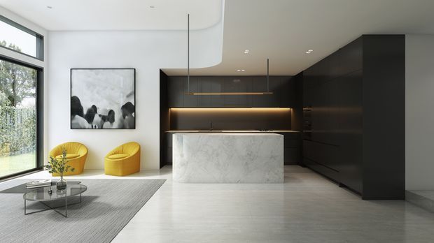 A refined open-plan kitchen and living area with a large white marble island, dark wood or charcoal cabinetry, integrated warm under-cabinet lighting, and a minimalist seating zone. Two sculptural mustard-yellow lounge chairs sit beside a glass coffee table on a neutral rug. Full-height glazing brings in garden views, while a curved white ceiling detail softens the contemporary interior.