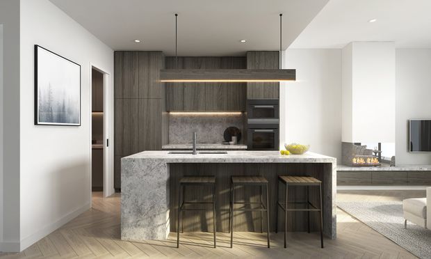 Contemporary open-plan kitchen with a large waterfall-edge stone island, three dark timber stools, dark wood cabinetry, integrated appliances, a linear pendant light, and pale timber flooring. A living area with a television and fireplace is visible beyond the kitchen.