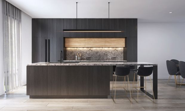 Contemporary open-plan kitchen dominated by a large dark wood island with a pale stone benchtop, matching full-height cabinetry, integrated warm wood cabinetry, and a textured stone backsplash. Black pendant lights hang over the island, with bar stools and a dining area visible beyond. Full-height sheer curtains and light flooring create a refined, neutral interior.
