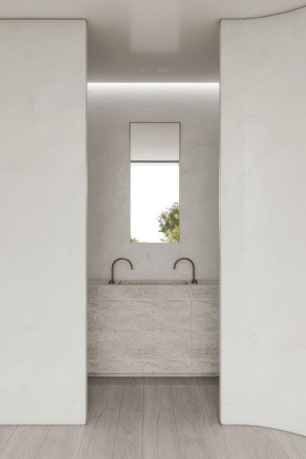 A minimalist kitchen or scullery view framed between two tall white cabinetry walls. The space features a compact stone or concrete-look benchtop with two curved dark metal faucets, integrated pale cabinetry, a narrow vertical window, concealed ceiling lighting, and light timber-look flooring. The composition is clean, symmetrical, and highly restrained.