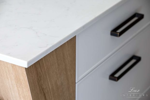 Close-up detail of built-in cabinetry featuring a white marble-look benchtop, light natural timber side panel, and pale grey drawer fronts with elongated dark metal handles. The image highlights refined kitchen or joinery detailing.