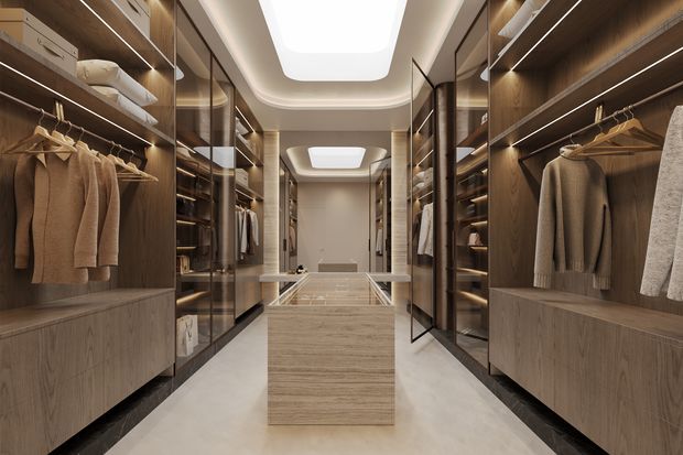 Luxurious walk-in wardrobe with symmetrical floor-to-ceiling timber-toned cabinetry, open illuminated shelving, hanging rails, drawers, glass-fronted storage, and a central island with a glass display top. Warm integrated LED lighting contrasts with the pale stone-look floor and sculptural recessed ceiling lights.