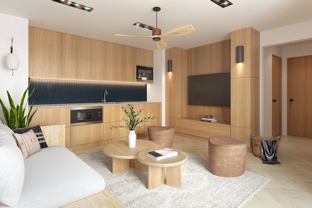 A bright open-plan living room with an integrated timber kitchen and media wall. Vertical-grain light timber cabinetry extends across the kitchen and TV joinery, complemented by a dark blue tiled splashback, warm wood-look flooring, layered round timber coffee tables, a pale sofa, upholstered ottomans, and a textured area rug. Recessed ceiling lights, pendant lighting, wall sconces, and a ceiling fan provide a contemporary, refined fit-out.