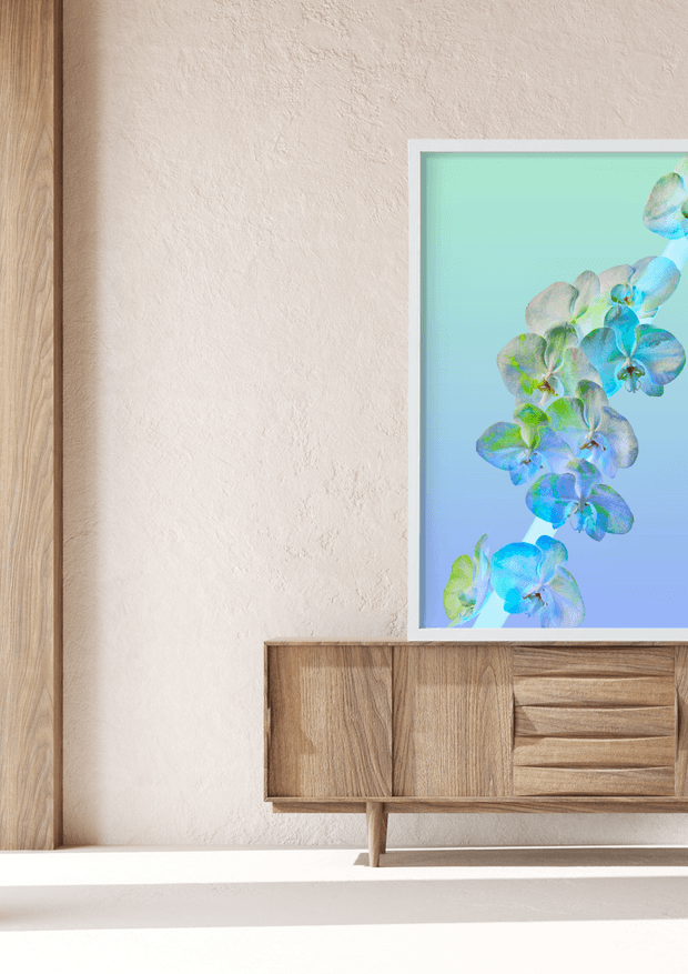 A bright, minimalist interior vignette featuring a light timber wall panel and matching mid-century-style sideboard with tapered legs and textured drawer fronts. A framed artwork of blue, green, and turquoise orchids hangs above the sideboard against a warm textured plaster wall, with strong sunlight creating crisp shadows.