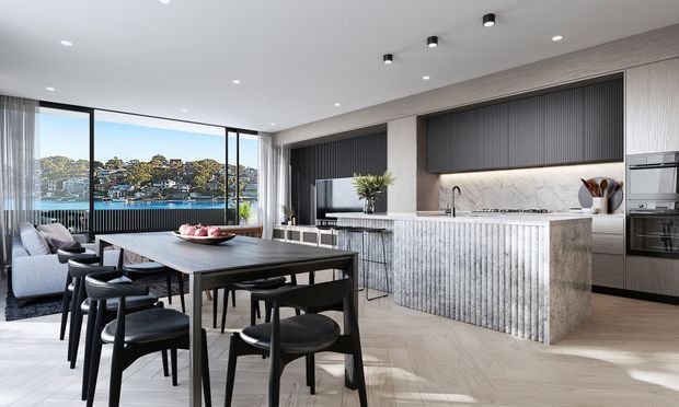 A sophisticated open-plan kitchen and dining area with a large island, dark ribbed cabinetry, veined marble-look splashback, and light timber flooring. A dining table with black chairs sits beside floor-to-ceiling glazing overlooking a waterfront residential landscape.