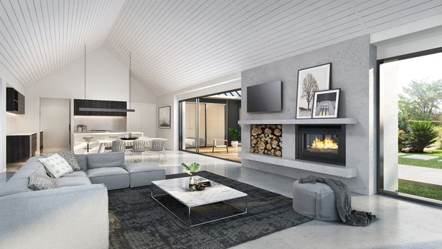 A bright, open-plan contemporary living room with a large light-grey sectional sofa, dark area rug, low rectangular coffee table, and a concrete-toned fireplace feature wall. The wall includes a built-in fireplace, firewood storage, television, and shelving. A white slatted vaulted ceiling, extensive glazing, and views to a landscaped garden create an airy indoor-outdoor connection, with the kitchen and dining area visible in the background.