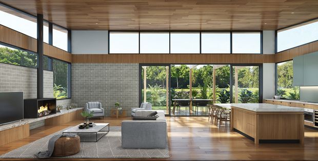 A spacious open-plan contemporary living and kitchen area with floor-to-ceiling glazing, a warm timber ceiling and timber flooring, exposed grey brick walls, a central fireplace, modern grey seating, and a large timber kitchen island. The glazing opens toward a lush planted outdoor setting and dining terrace.