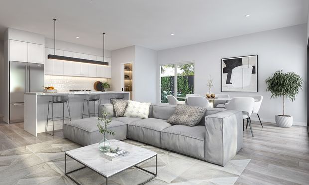 Bright open-plan contemporary interior combining a white kitchen with island seating, a living area with a large light-grey sectional sofa and marble-topped coffee table, and an adjacent dining area. The space features pale timber-look flooring, white cabinetry and walls, black linear pendant lighting, large windows, and restrained neutral decor.