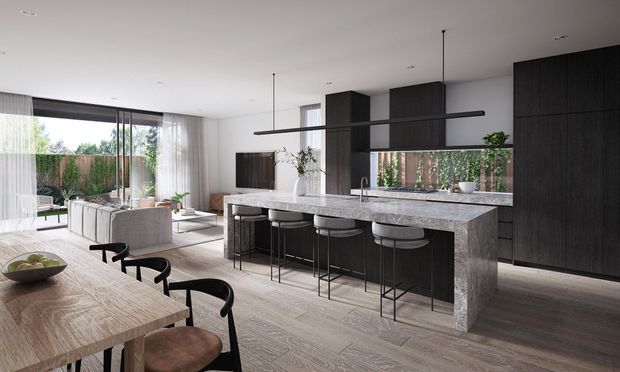 Open-plan contemporary kitchen and dining area with a large stone island, dark timber cabinetry, bar stools, and a light timber dining table. The space opens to a bright living area and landscaped outdoor setting through expansive glazing and sheer curtains. A slim linear pendant light spans the island.