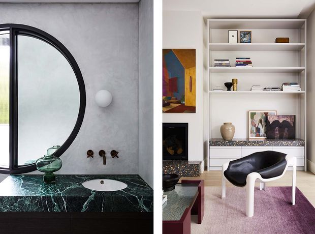 Split interior view showing a refined bathroom vanity on the left with a large black-framed arched window, textured grey wall, dark green veined stone benchtop, vessel basin and wall-mounted fittings. On the right is a sophisticated living room or study nook with built-in white shelving, a dark fireplace surround, artwork, books, sculptural decor and a black-and-white lounge chair on a muted pink rug.