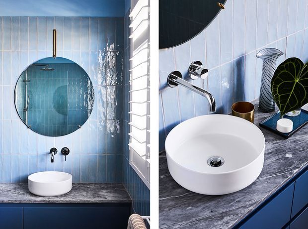 A stylish compact bathroom featuring glossy pale blue vertical wall tiles, a round wall-mounted mirror, a white freestanding basin on a dark veined stone vanity, chrome wall-mounted tapware, and blue fixed cabinetry. The image is presented as a split view showing the shower area and basin vanity, with bright louvred window shutters on the side.