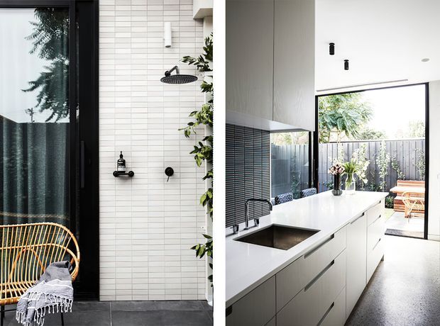 Split image showing a contemporary bathroom on the left and a bright modern kitchen opening to an outdoor patio on the right. The bathroom has white horizontal wall tiles, dark-framed glazing, black fixtures and a rattan chair. The kitchen features a long white island with integrated sink and dark tapware, streamlined white cabinetry, high ceilings, extensive glazing and a timber-fenced outdoor area beyond.