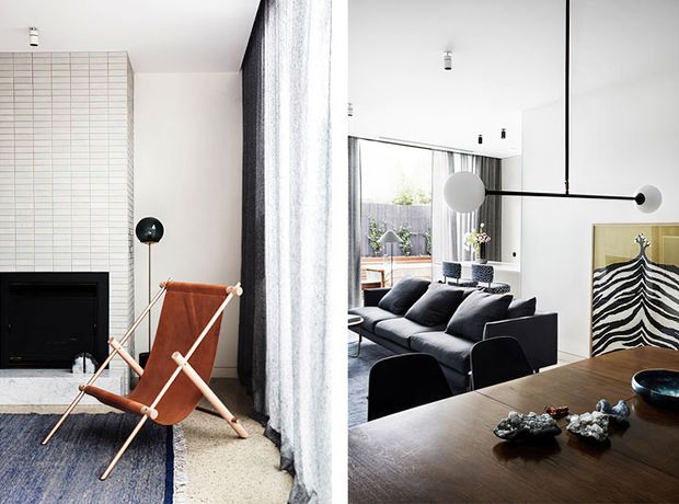 A bright, refined open-plan living and dining interior. The living area features a black sectional sofa, sculptural black pendant lighting, a tiled fireplace wall, a leather sling chair, and full-height curtains. The dining area has a dark timber table with black chairs, while a large mirror reflects the living space and a rear glazed opening leads toward an outdoor area. The palette is predominantly white, black, charcoal, brown, and natural timber.