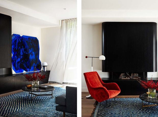 A split-view contemporary living room featuring a dramatic black curved fireplace surround, dark built-in cabinetry, a vivid blue abstract artwork, a red sculptural lounge chair, a black sofa, a glass coffee table, and a blue patterned rug. Sheer white curtains and a restrained white ceiling create contrast with the dark architectural elements and saturated furnishings.