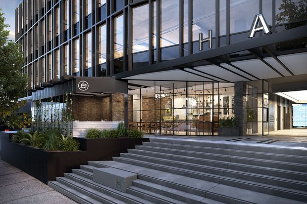 Contemporary multi-storey commercial building entrance with a dramatic broad flight of grey stone steps, glazed lobby frontage, dark metal framing, and vertical facade fins. The entry canopy carries large illuminated lettering, while landscaped planters soften the foreground. The interior lobby and reception/bar-like area are visible through the full-height glazing.