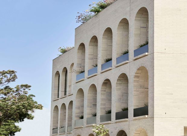 Exterior view of a multi-storey contemporary building with a pale masonry facade articulated by repeated tall rounded arches. Recessed balconies or openings contain dark planter boxes and sparse greenery, with additional rooftop planting visible. The composition is geometric and minimalist, set against a clear sky with trees at the edge of the frame.