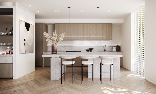 Bright contemporary kitchen featuring a large pale stone island with four slim bar stools, full-height light timber cabinetry, a subtle stone splashback, integrated appliances, and a herringbone timber floor. White walls, recessed lighting, and full-height louvred window coverings create an airy, refined interior. A partially visible drinks cabinet and artwork sit to the left.