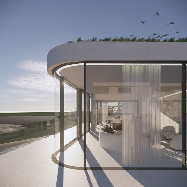 A contemporary curved-roof glass pavilion or residence viewed from an exterior terrace. Full-height glazing with slim dark frames wraps around a bright interior furnished with pale rounded seating and sheer curtains. The smooth white roof has a planted green edge, while long shadows fall across the pale terrace. Water and a low railing are visible beyond the building, with birds in the sky.