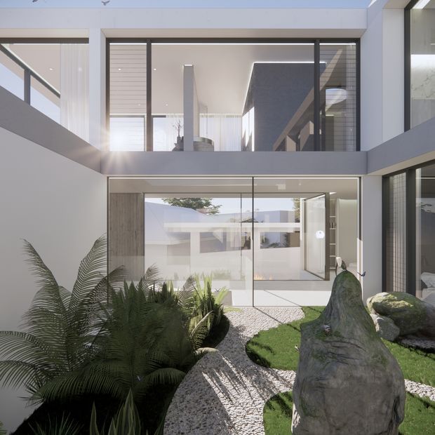 A bright contemporary courtyard viewed from within or beside a modern multi-level residence. White rendered walls, extensive dark-framed glazing, and strong geometric forms surround a landscaped courtyard with gravel, clipped lawn, large rocks, and lush fern planting. An upper-level void or bridge overlooks the courtyard, creating a layered indoor–outdoor connection.