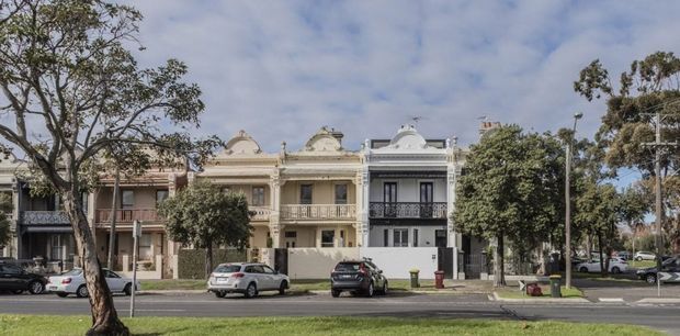 Street-level exterior view of a row of attached heritage-style urban residences. The facades feature ornate classical detailing, decorative parapets, balconies, columns, rendered walls, and varied neutral finishes, with mature street trees and parked cars in the foreground.