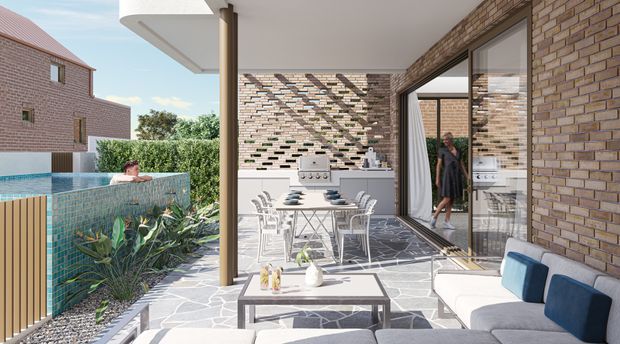 Contemporary covered outdoor entertaining area beside a swimming pool, with a built-in barbecue kitchen, dining table, lounge seating, large sliding glass doors, and exposed brick walls. The space uses irregular dark stone paving, timber screening, and a perforated brick feature wall, opening onto landscaped planting and the pool.