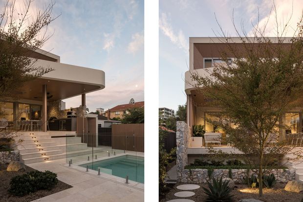 A split-view exterior photograph of a contemporary multi-storey residence at dusk, showing a curved white projecting roof or canopy, extensive glazing, an elevated terrace, broad stone steps, glass pool fencing and a compact rectangular swimming pool. The landscaped garden includes layered stone retaining walls, gravel, sculptural succulents, shrubs and stepping stones. The second view shows the rounded balcony edge, warm interior lighting and pale rendered facade.