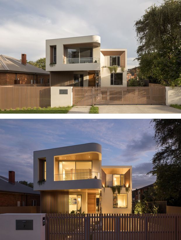 Composite day-and-dusk photographs of a contemporary multi-storey urban residence. The house has a sculptural rounded balcony volume, rectilinear upper-level forms, large glazed openings, warm timber-look vertical screening, a timber front door, and a vertical slat front fence with pedestrian and vehicle gates. Adjacent brick homes and mature trees frame the suburban streetscape.
