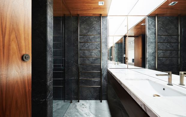 Contemporary bathroom with a long double vanity, white stone benchtop, wall-to-wall mirror, dark stone shower surround, timber cabinetry and warm timber ceiling. The space has a refined, high-contrast material palette and integrated recessed lighting.