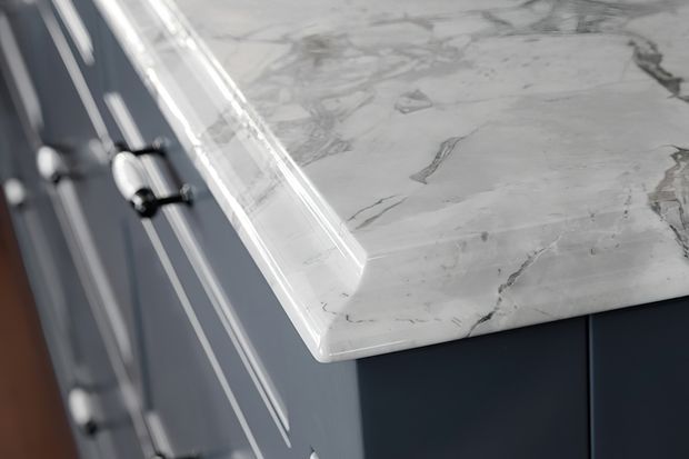 Close-up detail of a dark blue-grey built-in cabinet with small round metal knobs and a thick white marble-look benchtop featuring prominent grey veining and a rounded eased edge.