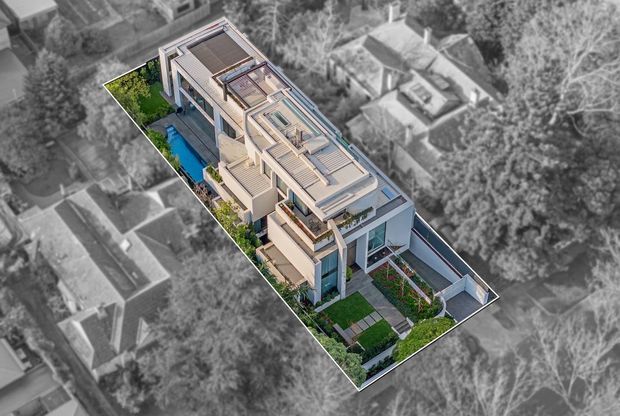 Aerial architectural rendering of a long, narrow contemporary multi-level residence on a landscaped urban site. The highlighted property features a flat roof with multiple rooftop terraces or glazed roof structures, extensive balconies, pale rendered walls, dark-framed glazing, landscaped gardens, and a narrow blue swimming pool. Surrounding buildings and trees are shown in grayscale to emphasize the featured property.