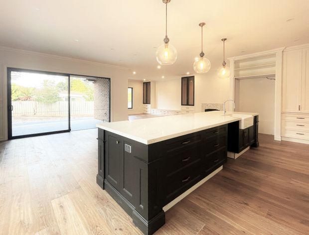 Bright open-plan kitchen with a large black island and white stone benchtop, extensive white cabinetry, dark timber flooring, pendant lighting, and sliding glass doors opening to an outdoor area.