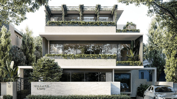 Modern multi-storey residential building with a pale textured facade, broad horizontal floor plates, extensive floor-to-ceiling glazing, rooftop terraces, and abundant integrated planter greenery. A low stone entrance wall and landscaped frontage define the street-facing facade, with a driveway and parked car at the side.