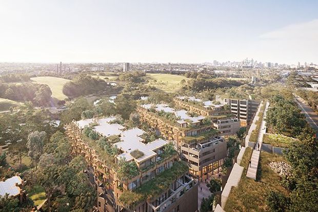 Aerial architectural rendering of a large, multi-storey contemporary development integrated into a leafy urban parkland setting. The complex features flat-roofed buildings, extensive rooftop planting and terraces, landscaped courtyards, and a prominent elevated pedestrian walkway or ramp. A dense city skyline is visible in the distance.