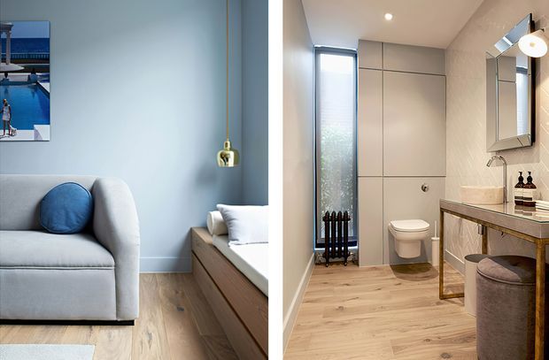 Split image showing a softly styled bedroom on the left and a contemporary bathroom on the right. The bedroom features pale blue walls, a light upholstered bed or sofa, blue cushion, timber flooring, built-in timber joinery and a brass pendant. The bathroom has a wall-hung toilet, large-format light wall tiles, timber-look flooring, a slim vertical window with radiator, stone-look vanity, framed mirror and upholstered stool.