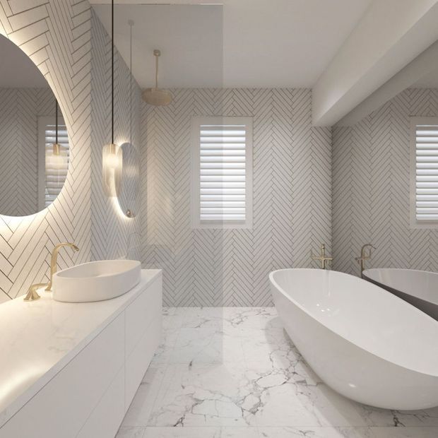 Bright, refined contemporary bathroom featuring a freestanding white bathtub, vessel basin on a floating vanity, marble-look flooring, and pale herringbone wall tiling. Brass tapware, round mirrors, wall sconces, and shuttered windows add warm detail to the predominantly white interior.