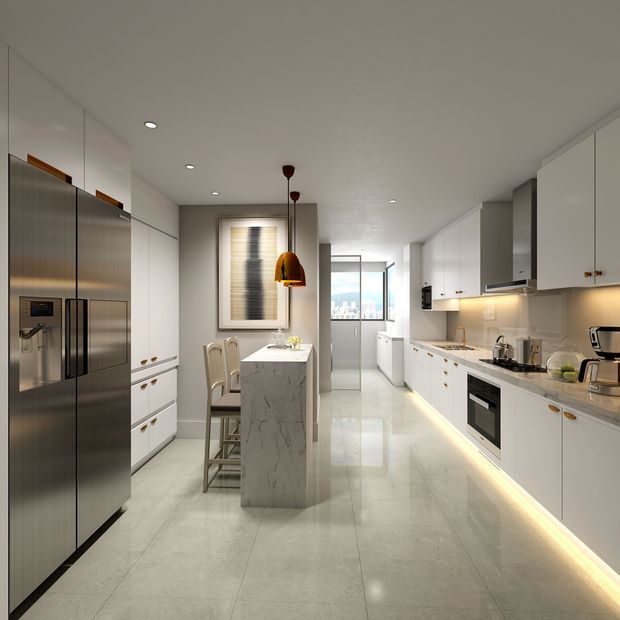 A bright, narrow galley-style kitchen with white full-height cabinetry, integrated appliances, a large stainless-steel refrigerator, and a central marble-look island with seating. Glossy pale floor tiles, under-cabinet lighting, pendant lights, and a window at the far end create a clean, contemporary interior.