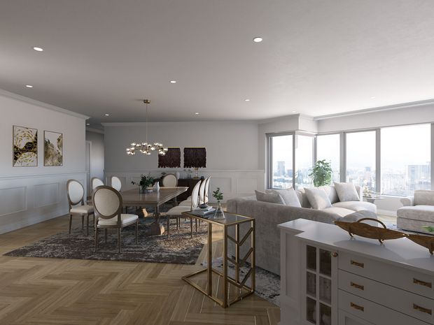 Bright, refined open-plan dining and living room with large corner windows overlooking a city skyline. The space features white decorative wall panelling, a neutral upholstered sofa, an oval dining table with upholstered chairs, a crystal-style pendant light, patterned area rugs, and herringbone timber flooring. A white built-in or freestanding storage unit with brass hardware sits in the foreground.