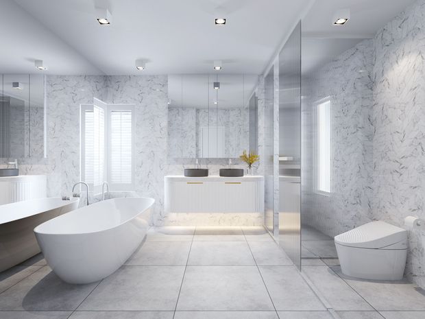 A bright, contemporary luxury bathroom featuring a freestanding white bathtub, wall-mounted double vanity, large mirrors, a glass-enclosed shower, and a concealed-style toilet. White marble-look wall surfaces and large pale floor tiles create a clean, monochromatic interior with integrated recessed lighting and plantation shutters.