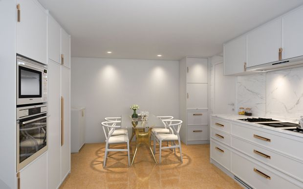 Bright, compact white kitchen and dining area with floor-to-ceiling cabinetry, integrated stainless-steel appliances, a marble-look splashback, white shaker-style joinery with brass pulls, and a central glass dining table surrounded by white wire-frame chairs. Recessed ceiling lights create an even, refined contemporary interior.