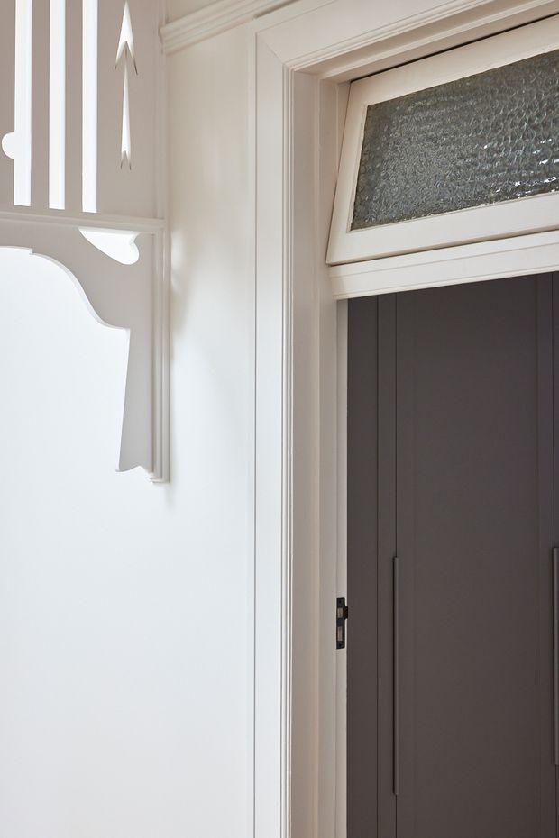 Close-up interior view of a refined traditional entryway, featuring a dark double door with long vertical handles, a textured glass transom window, and ornate white-painted timber trim and decorative wall panelling.