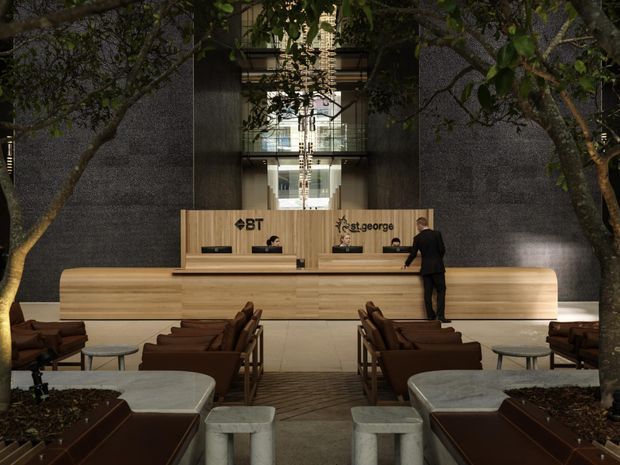 A dramatic commercial reception lobby with a long curved timber reception desk, integrated workstations, and visible BT and St.George branding. Dark textured stone or concrete walls frame a tall glazed atrium with suspended linear lighting. Leather lounge seating, low tables, raised planter beds, and indoor trees create a refined waiting area in front of the desk.
