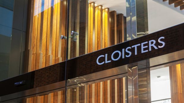 Interior architectural view of a contemporary commercial entrance or lobby featuring a prominent illuminated “CLOISTERS” sign, dark brickwork, extensive vertical timber wall cladding, glass, and reflective metal surfaces.